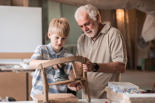 A grandfather teaches his grandson how to fix furniture in his carpenter workshop. They work together, sharing tools and skills, as the grandfather passes on his knowledge.