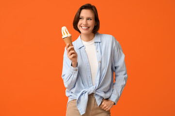 Happy young woman with sweet ice-cream in waffle cone on orange background
