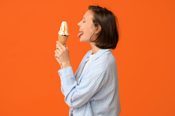 Beautiful young woman with sweet ice-cream in waffle cone showing tongue on orange background