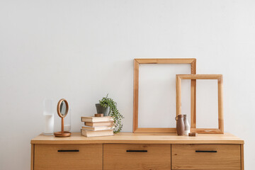 Books with plant and decor on wooden commode near light wall