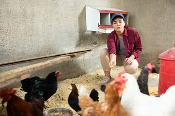Young female farmer kneeling to feed hens