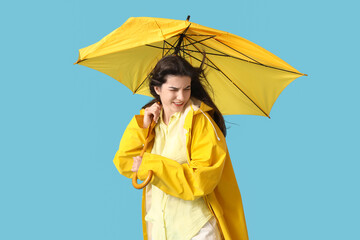 Young woman in raincoat with broken umbrella and strong wind on blue background