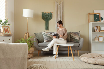 Young woman reading magazine on sofa with hanging wall tapestries in living room