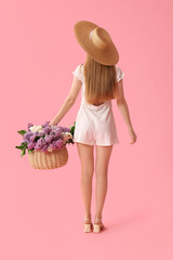 Beautiful young woman with wicker basket of lilac flowers on pink background, back view