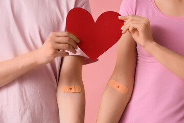 Blood donors with applied patches and paper heart on pink background, closeup