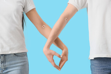 Blood donors with applied patches making heart gesture on blue background, closeup