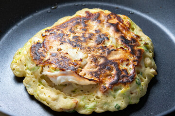 フライパンでお好み焼きを焼く調理シーン。
