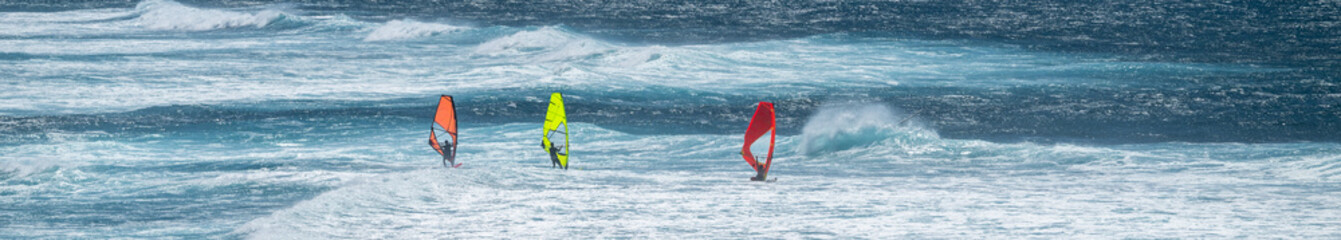 Three colorful windsurfers, red, orange, and yellow, racing in the wind on the Pacific Ocean off...