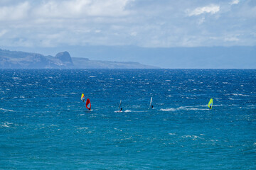 Colorful wind surfers racing in the wind on the Pacific Ocean off the coast of Maui at Hookipa...