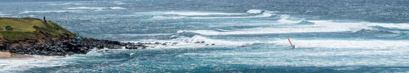 Man on a wind surfer with red sail riding the wind on the Pacific Ocean off the coast of Maui at Hookipa Beach, Hawaii

