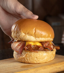 A hand reaching a big hamburger with brioche bread, meat, cheddar cheese, barbecue sauce, and...
