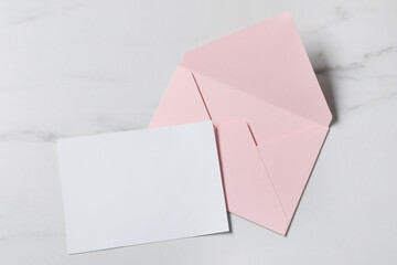 Blank sheet of paper and letter envelope on white marble table, top view