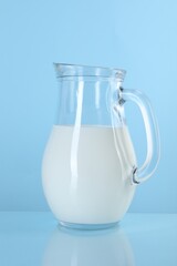 Jug of fresh milk on light blue background