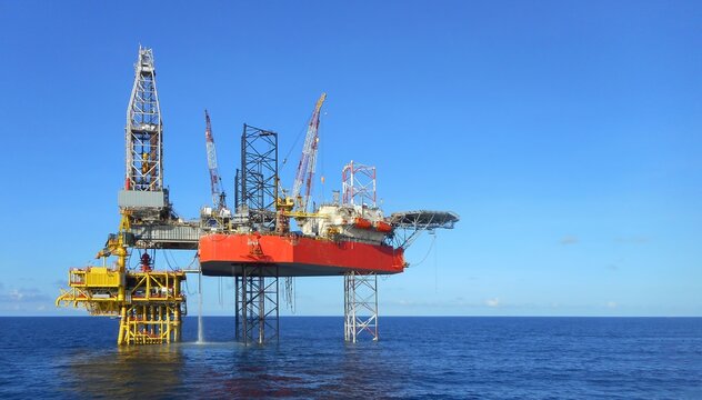 Drilling rig operate in well slot platform showing derrick, cranes and helipad with clear blue sky background. High resolution industry image