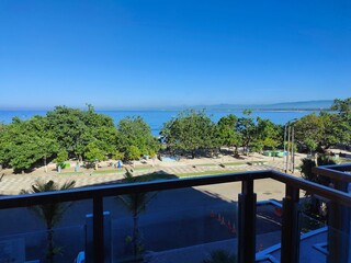 Sunny Beachfront View from Hotel Balcony with Bright Sunlight and Clear Blue Sky