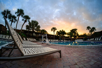 Sundown Oasis: Low-Angle View of Pool Patio Furniture, Silhouetted Palm Trees, and Sunset-Adorned Sky