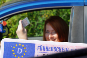 Eine junge Frau im Auto zeigt den Führerschein