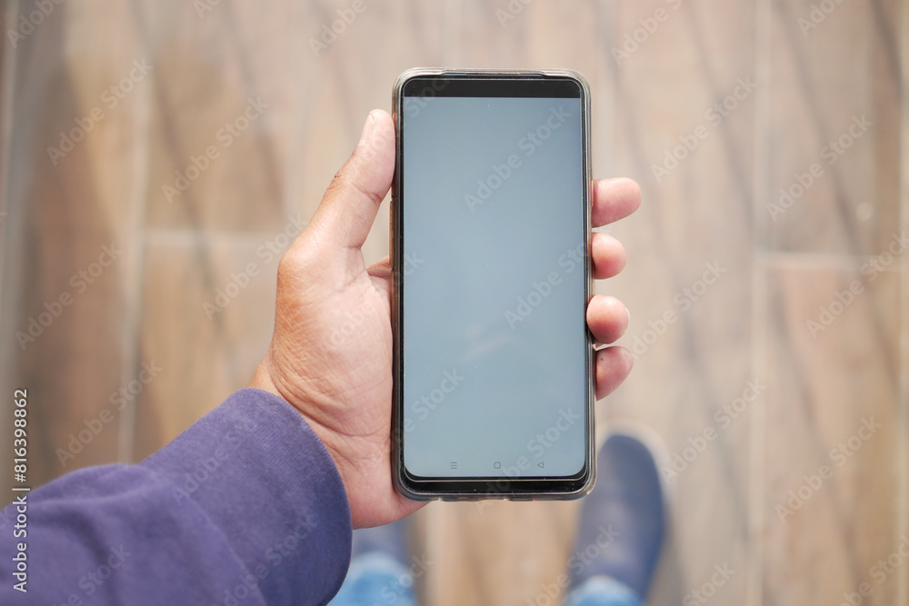 Wall mural pov shot of holding smart phone with white screen against wooden floor