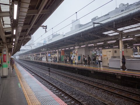 many passengers waiting for the train coming at the platform in rainy day in tokyo