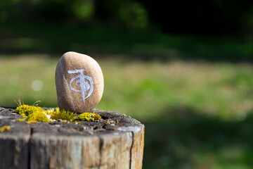An image of a healing Reiki symbol painted on a beige stone and resting on a moss covered fence post. 