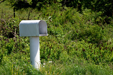 An image of a single white rural mailbox on the side of a rural country road. 