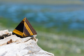 An image of a healing tigers eye pyramid crystal resting on a sun bleached driftwood log. 