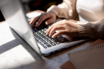 Close-up image of a woman typing on keyboard, working on her laptop computer at a table indoors.