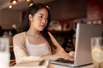 Young focused Asian woman working on her laptop computer while sitting in a coffee shop.
