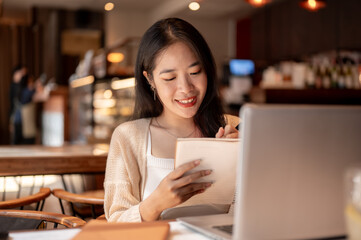 A young positive Asian female college student studying online and doing homework at a coffee shop.