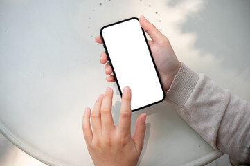 A close-up image of a woman sits outdoors on a sunny day and uses her smartphone, typing on screen.