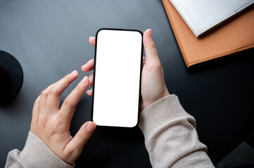 Top view image of a woman holding a smartphone white-screen mockup over an office desk workspace.