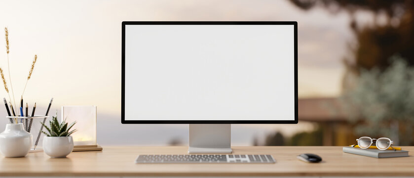 A PC computer mockup and accessories on a wooden desk with a blurred background of an outdoors.