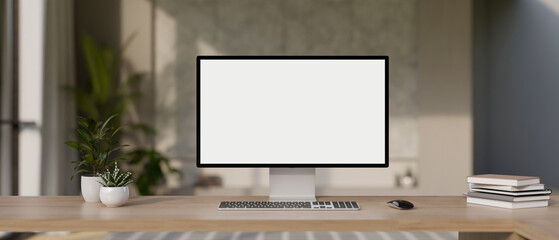 A desktop computer mockup and accessories on a wooden desk in a modern office room.