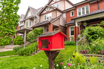 A free book exchange box, bright red,  on a residential street shot in the toronto beaches neighbourhood in spring room for text
