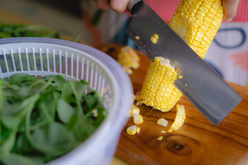 woman cutting corn in the wooden board, home cooking concept