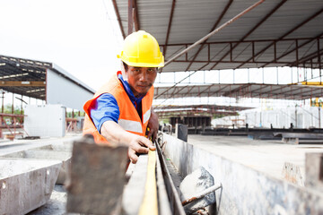 Construction engineer using measuring tape to measure a concrete bar.