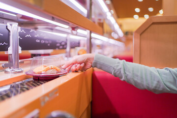 Happy Asian woman eating Sushi at modern Japanese conveyor belt Sushi bar.
