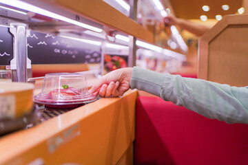 Happy Asian woman eating Sushi at modern Japanese conveyor belt Sushi bar.