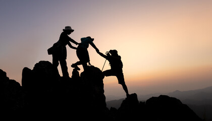 Fototapeta premium Silhouette of teamwork of three mountain climbers helping each other on the mountain top, climbing team, Hiking, friendship as a team, helping each other, helping in the mountains, sunrise.