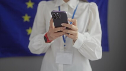 A professional woman using a smartphone with a european union flag in the background indoors - Powered by Adobe