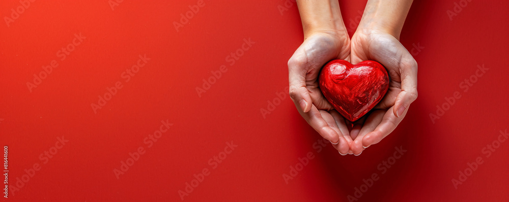 Poster against a minimalist, solid-colored background, two hands present a bright red heart, creating a str