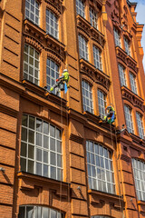 Window cleaners wash windows at height on the facade of a brick building.