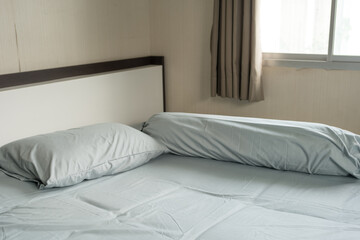 Blue bed with one pillows and one bolsters next to window. Loneliness in a bedroom