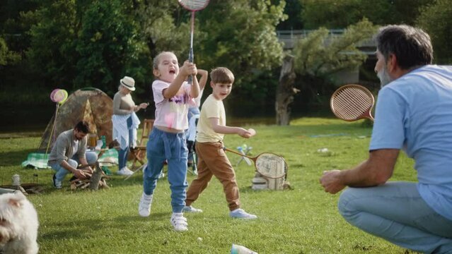 Grandfather and granddaughter play bagminton on camping in nature with family