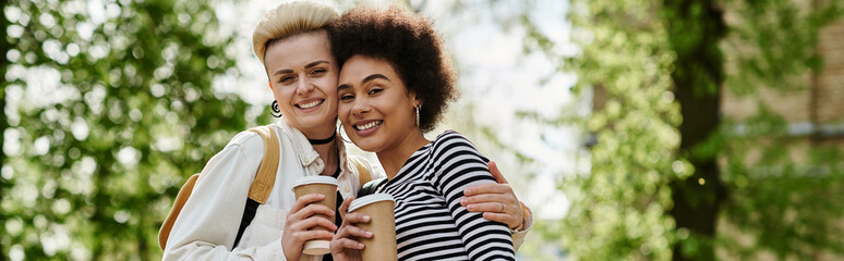 Two young women, multicultural lesbian couple, hugging each other warmly in a park setting,...