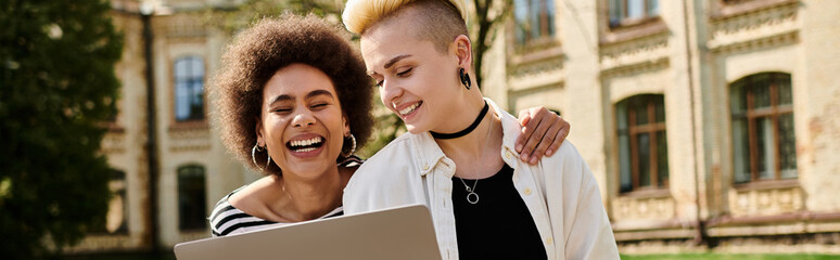 Two women joyfully smiling as they collaborate on a laptop together.