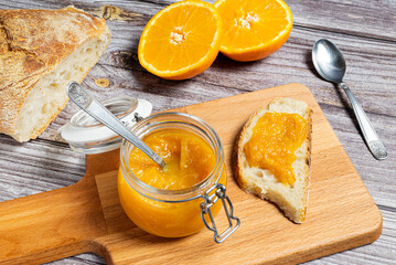 Delicious homemade orange jam in a glass jar on a wooden cutting board. Healthy breakfast with homemade orange jam