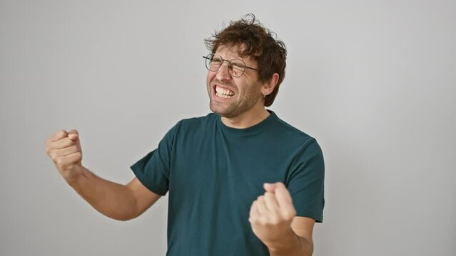 Excited young hispanic man wearing glasses, standing ecstatically as a winner, arms raised in a triumphant success gesture. he's screaming with joy, isolated on a white background.