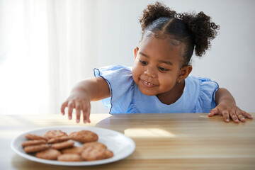 African child girl picking and eating chocolate cookies or biscuits from dish