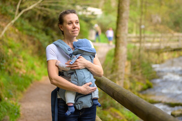 Happy woman looking to distance while holding and carrying it in a baby carrier